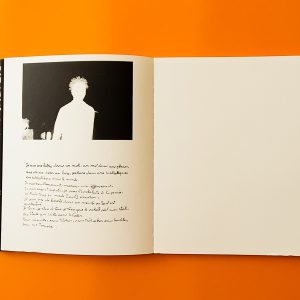 livre ouvert sur fond orange avec une page blanche et une page avec un homme et une écriture dessous